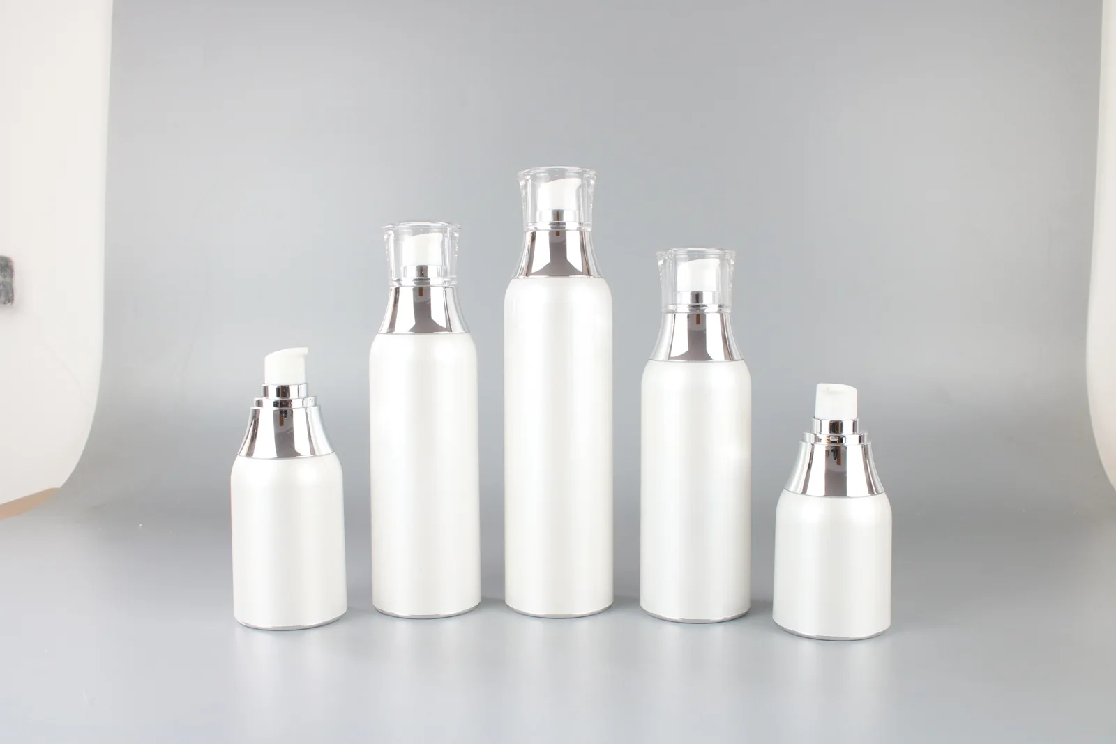 Five white cosmetic pump bottles in different proportions